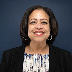 Nancy Hill smiles into the camera against a dark blue background.
